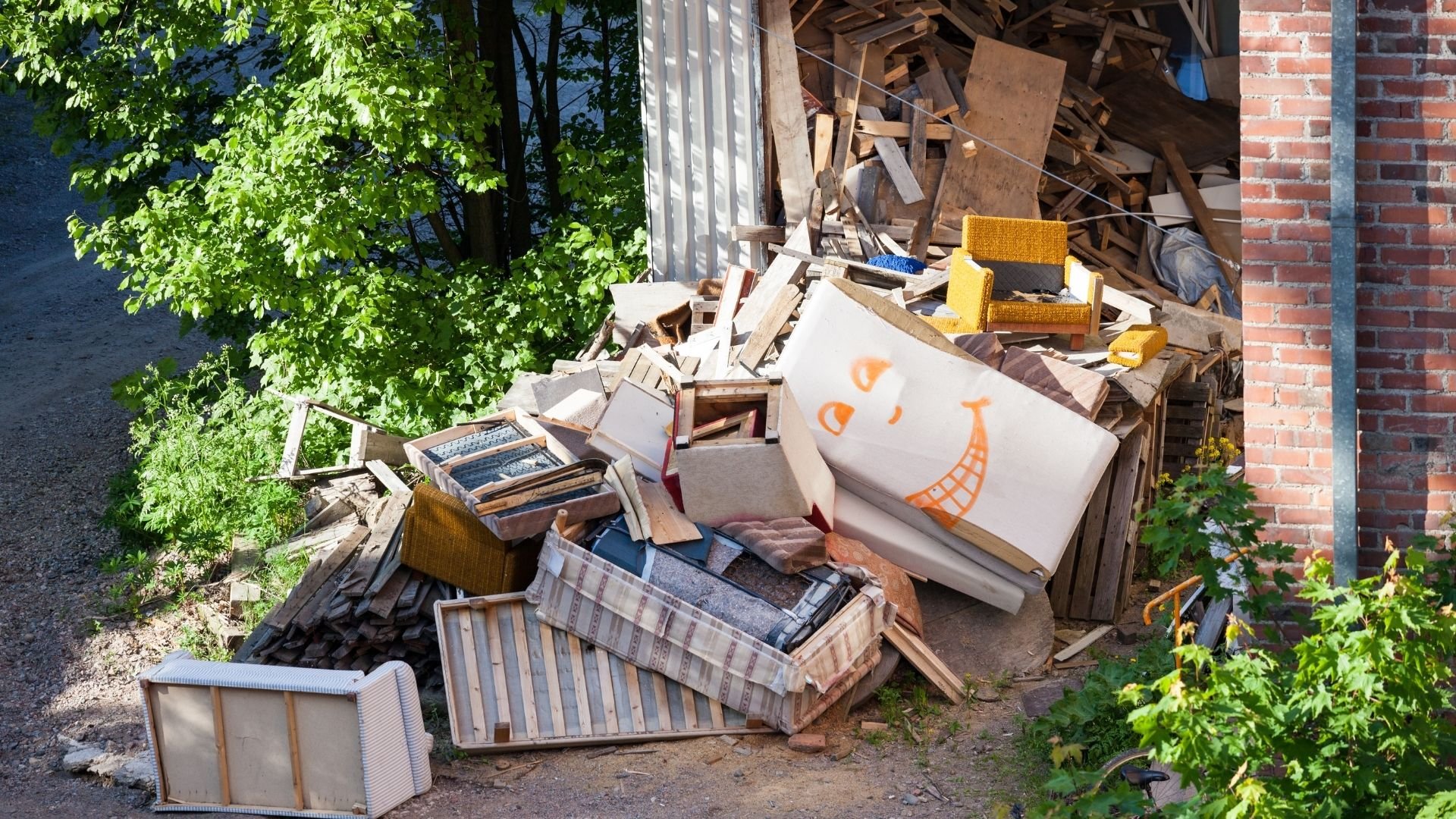 Pile of discarded furniture and waste materials in alley beside brick building