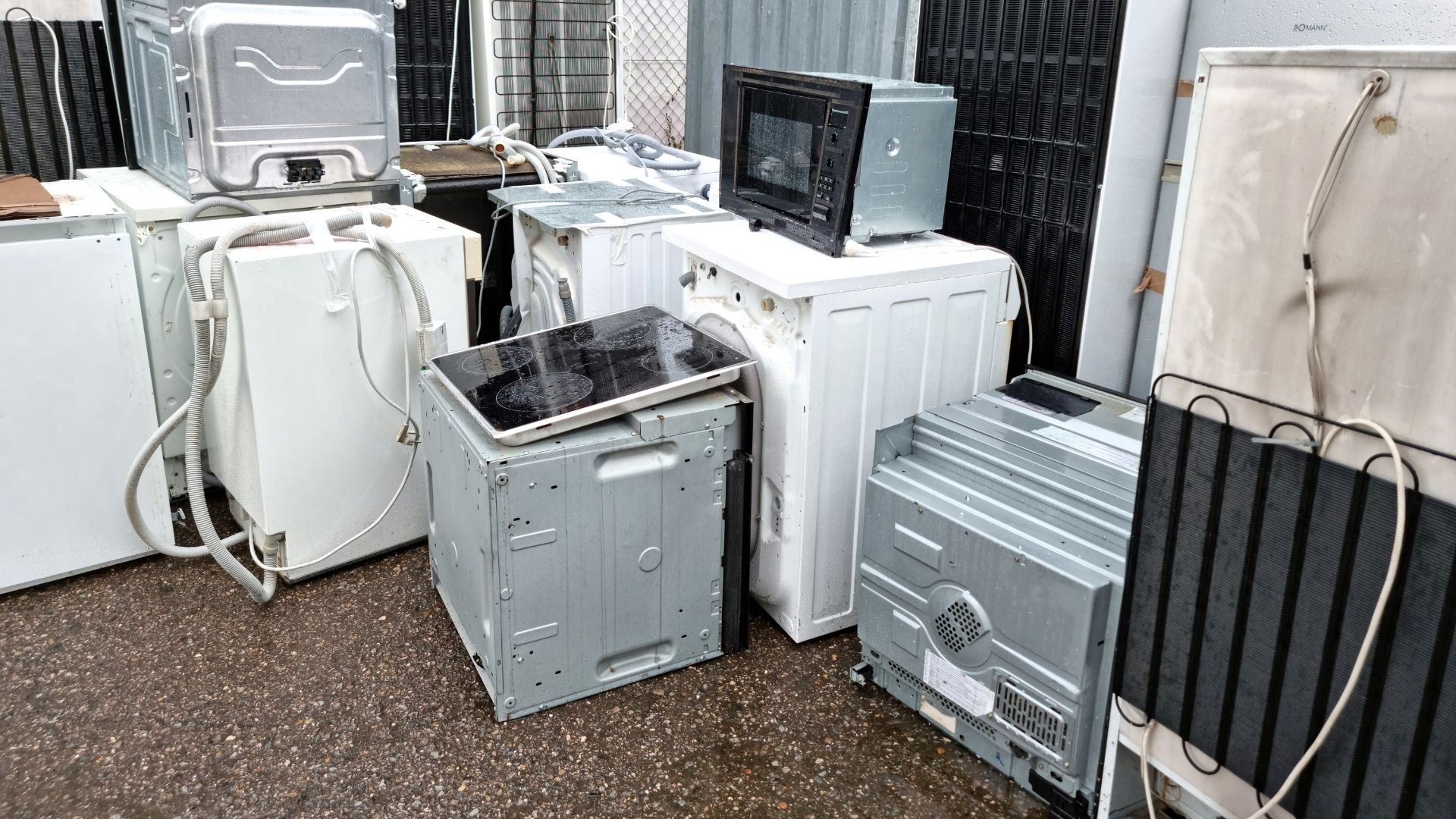 Discarded white appliances including washing machines, dryers, and refrigerators in a recycling yard.