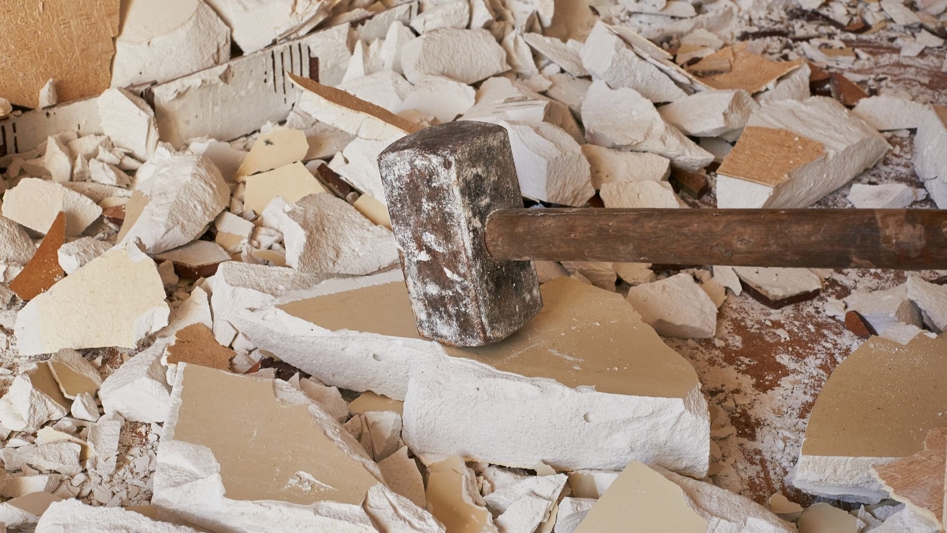 Hammer and chisel resting on debris pile of broken white and tan plaster