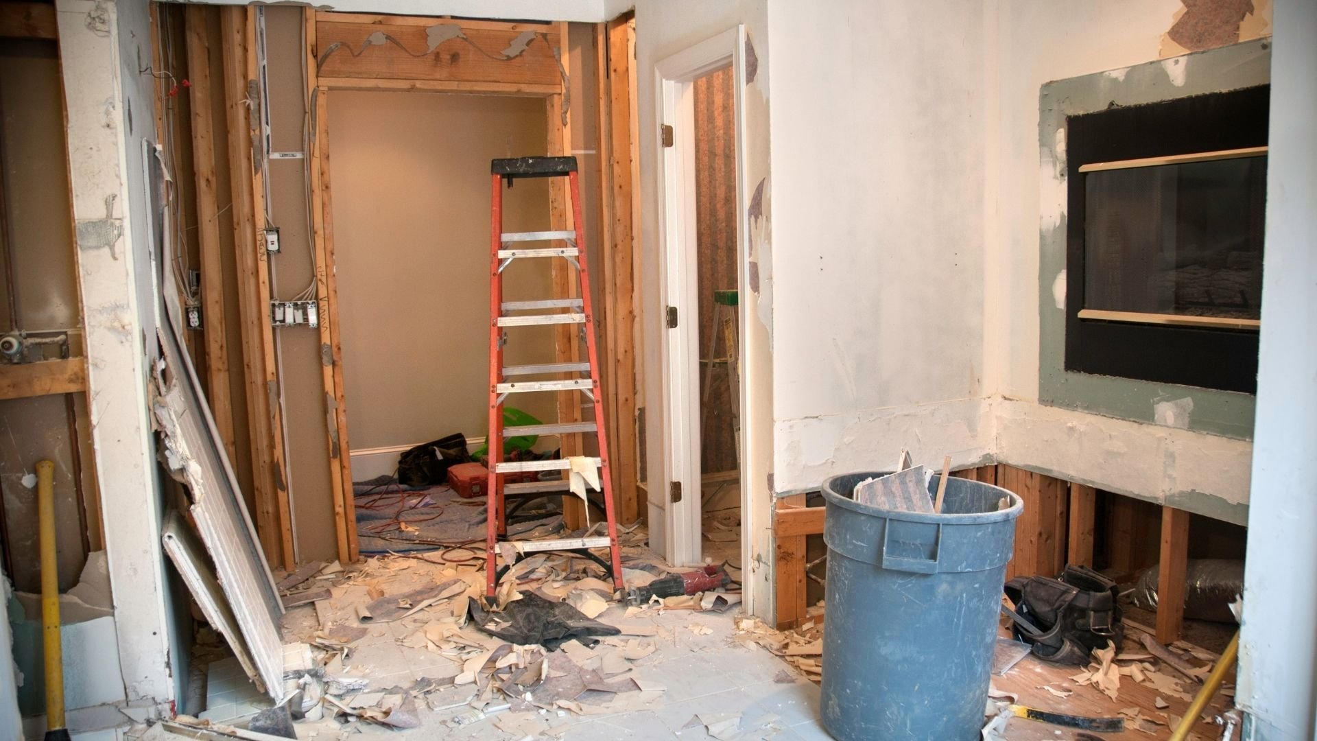 Interior home renovation in progress with red ladder and construction debris scattered on floor.