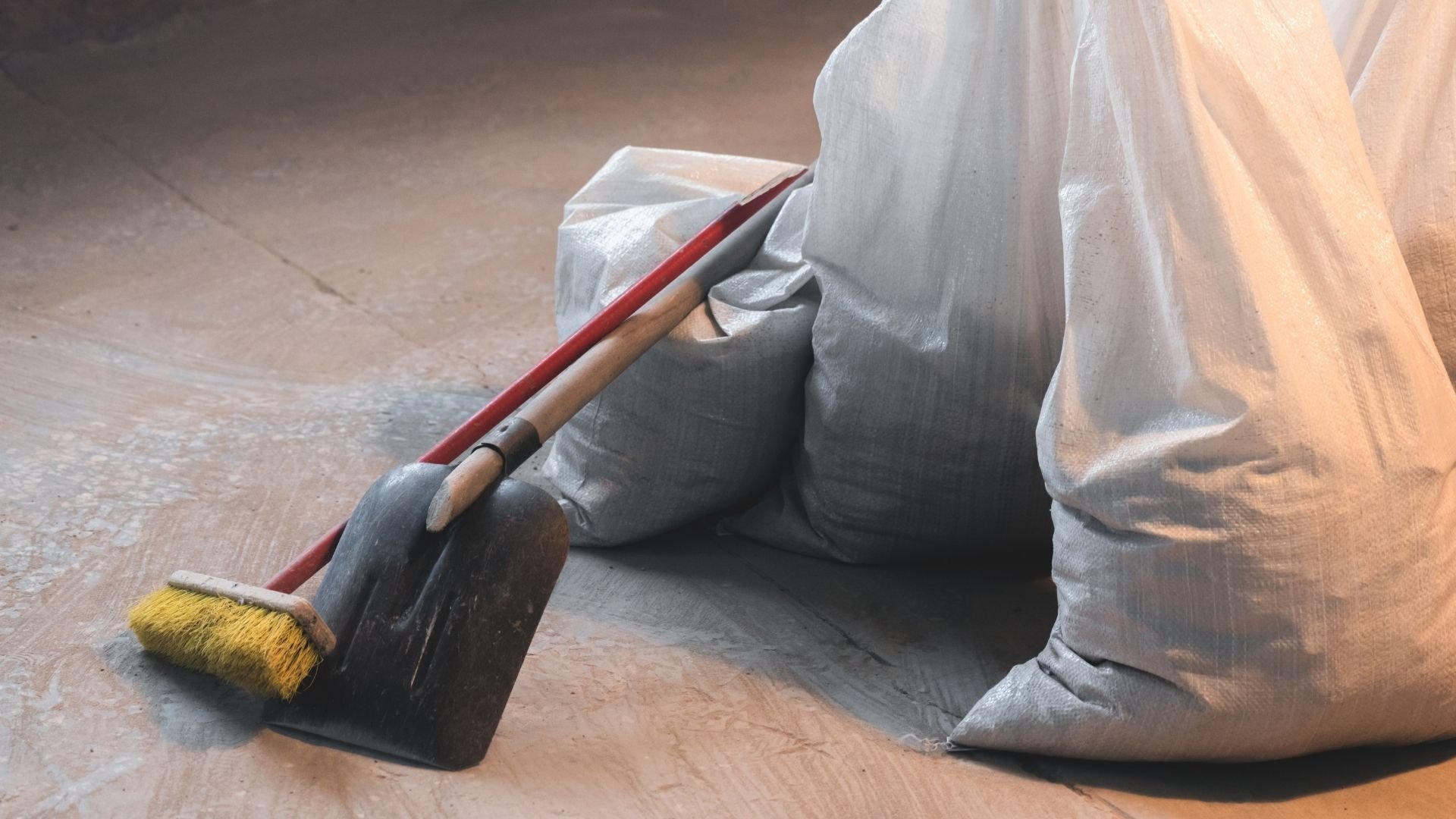 Worker in light-colored clothing holding paint brush with yellow bristles on floor